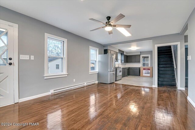 unfurnished living room featuring a baseboard radiator, stairway, hardwood / wood-style floors, a ceiling fan, and baseboards