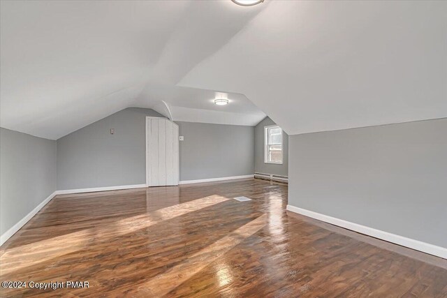 additional living space featuring lofted ceiling, a baseboard heating unit, wood finished floors, and baseboards