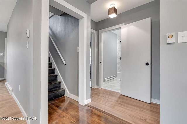 staircase featuring a baseboard heating unit, wood finished floors, and baseboards