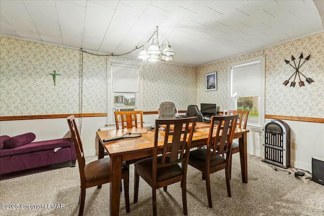 carpeted dining space with a wainscoted wall, an inviting chandelier, and wallpapered walls