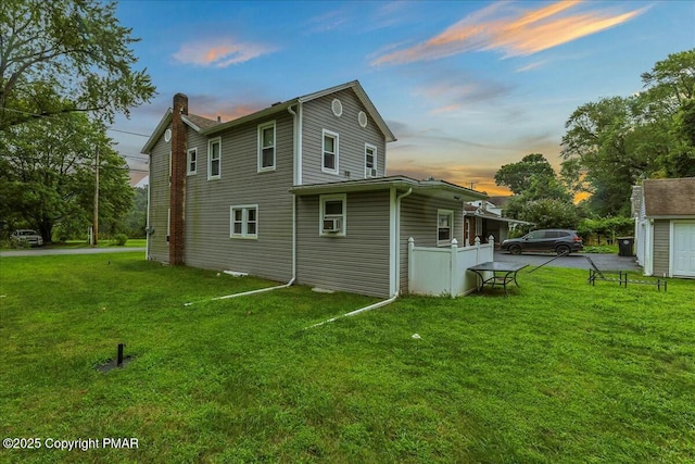 rear view of house with a chimney, cooling unit, and a lawn