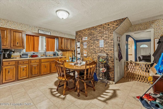 kitchen with wallpapered walls, brown cabinets, light countertops, a textured ceiling, and a sink