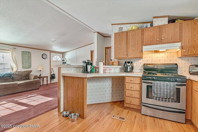 kitchen with stainless steel gas range oven, under cabinet range hood, a peninsula, open floor plan, and light countertops