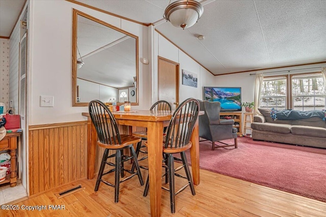 dining area with a textured ceiling, visible vents, light wood-style floors, vaulted ceiling, and wainscoting