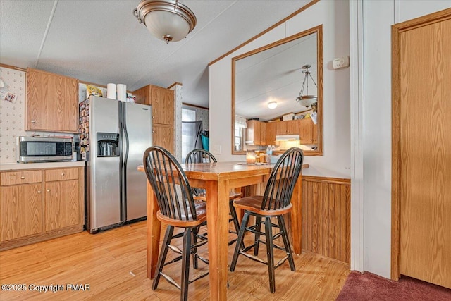 kitchen with light wood finished floors, wainscoting, appliances with stainless steel finishes, light countertops, and under cabinet range hood