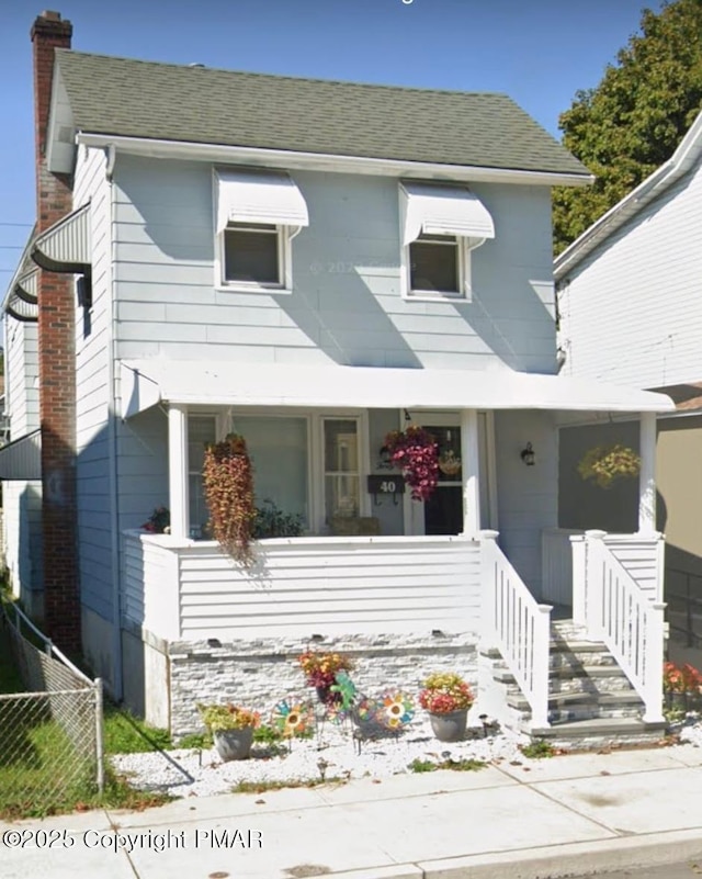 view of front of house featuring covered porch, a shingled roof, a chimney, and fence