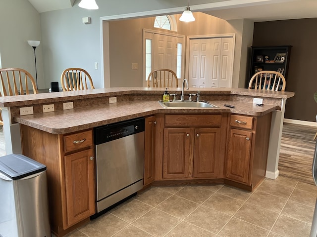 kitchen featuring dishwasher, a sink, brown cabinetry, hanging light fixtures, and light tile patterned floors