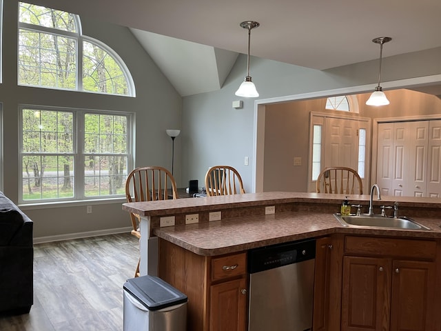 kitchen with stainless steel dishwasher, a sink, dark countertops, lofted ceiling, and pendant lighting