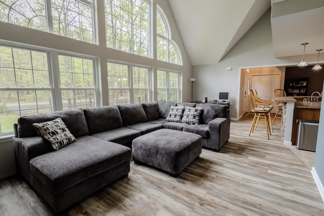 living room featuring high vaulted ceiling, light wood finished floors, and baseboards