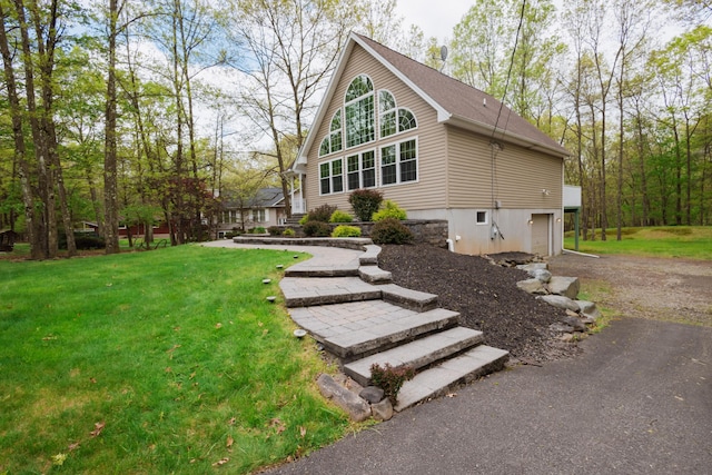 view of side of home with asphalt driveway, a garage, and a yard