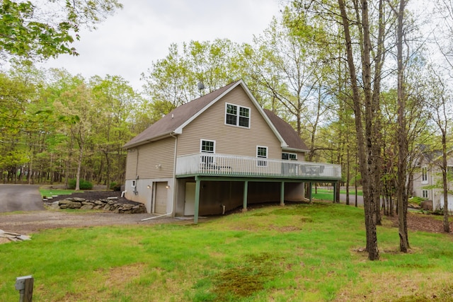 rear view of property with an attached garage, a deck, a yard, and driveway