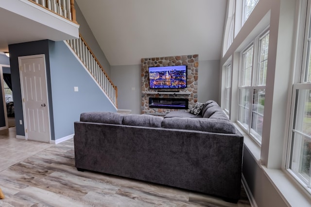 living room featuring a stone fireplace, high vaulted ceiling, stairs, and wood finished floors