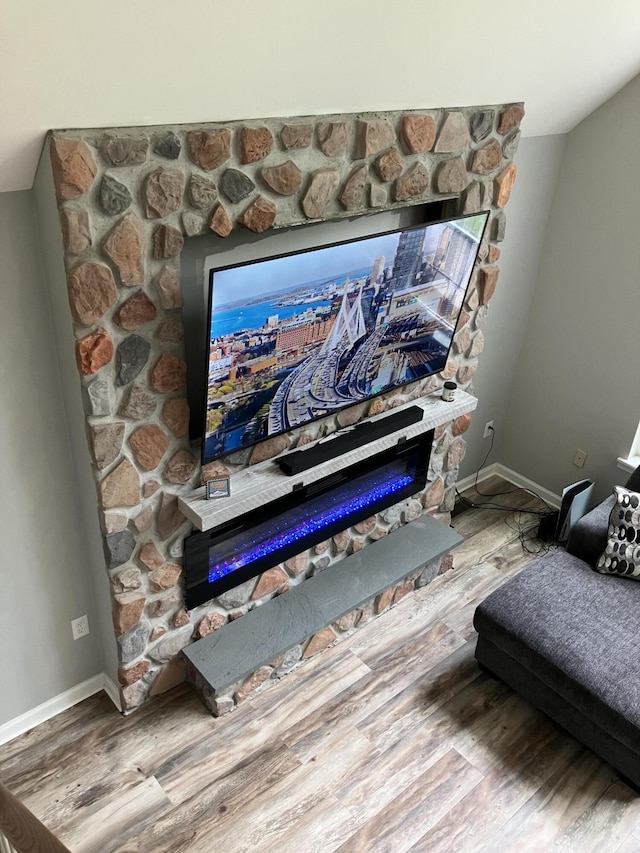 detailed view of a glass covered fireplace, wood finished floors, and baseboards