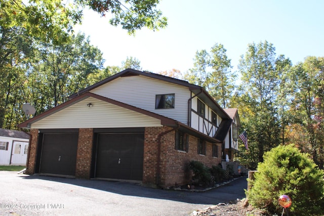 view of side of home with a garage, aphalt driveway, and brick siding