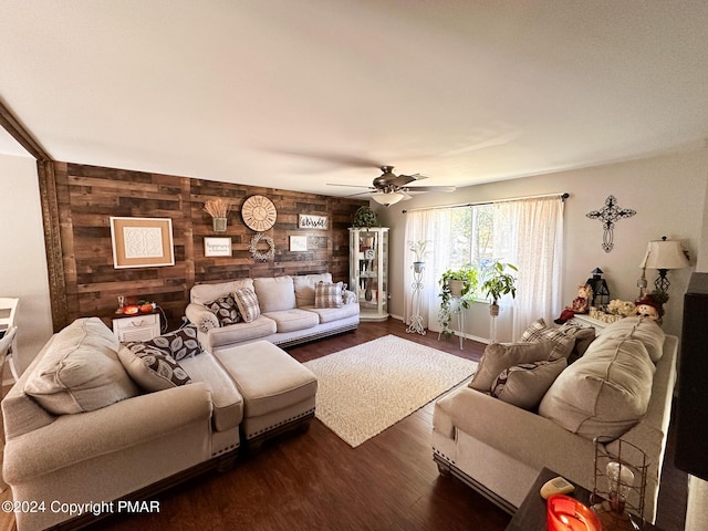 living room featuring dark wood-style flooring, wood walls, a ceiling fan, and an accent wall