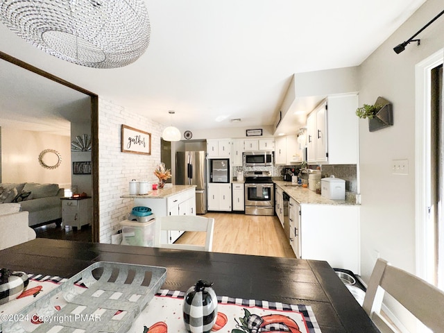 kitchen with decorative backsplash, appliances with stainless steel finishes, white cabinets, brick wall, and light wood-type flooring