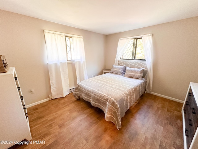 bedroom featuring a baseboard heating unit, wood finished floors, and baseboards