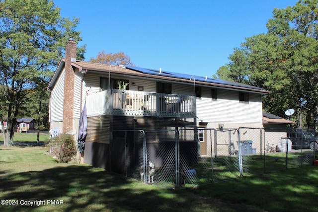 rear view of house with solar panels, a lawn, a gate, fence, and a deck