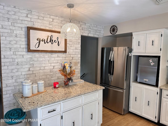 kitchen with light wood finished floors, brick wall, white cabinets, and freestanding refrigerator