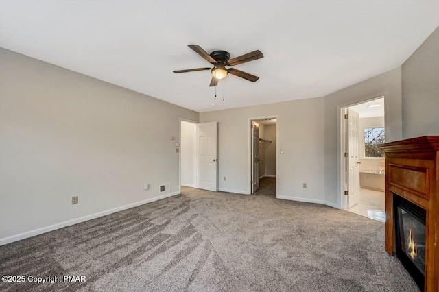 unfurnished bedroom featuring baseboards, visible vents, a glass covered fireplace, a spacious closet, and carpet flooring