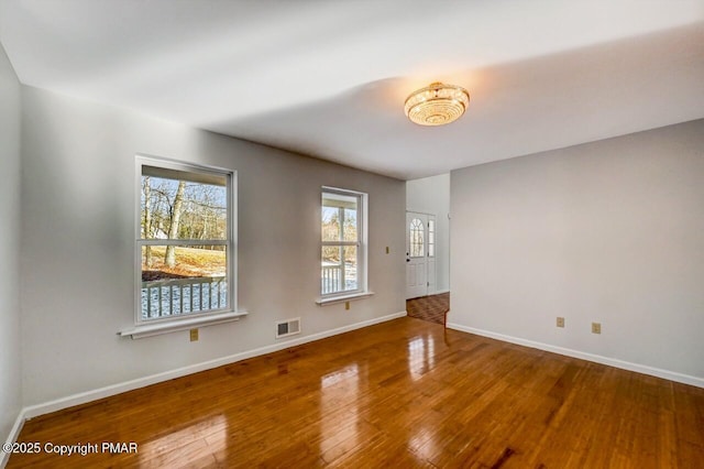 empty room featuring wood-type flooring, visible vents, and baseboards