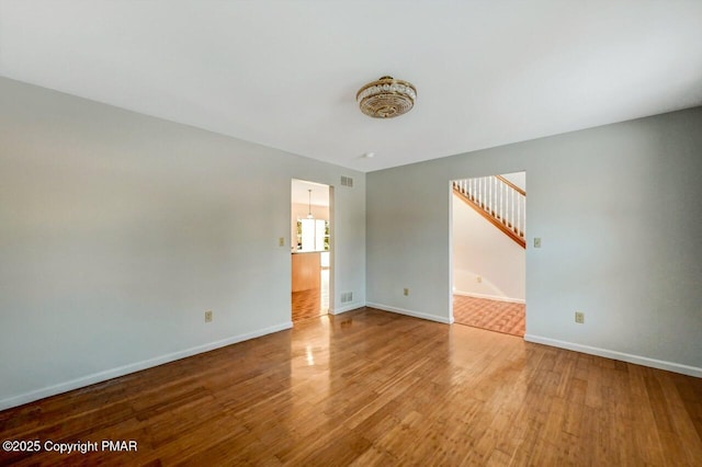 spare room with visible vents, stairs, baseboards, and wood finished floors