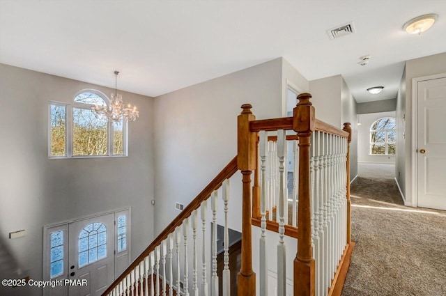 stairs with plenty of natural light, carpet flooring, visible vents, and a notable chandelier