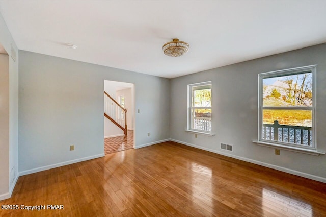 spare room featuring stairs, wood-type flooring, visible vents, and baseboards