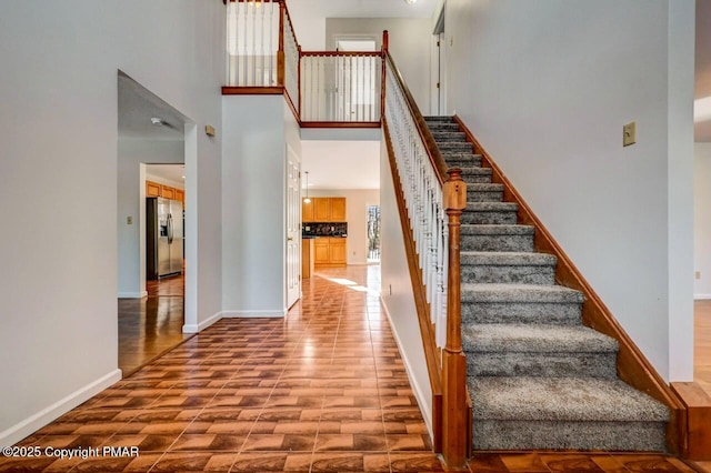 staircase featuring a towering ceiling and baseboards