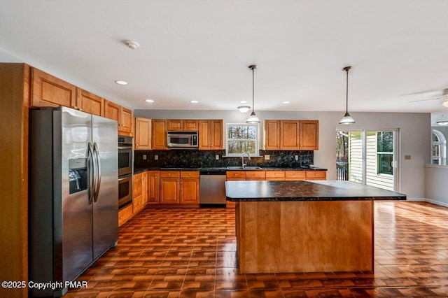 kitchen with dark countertops, decorative backsplash, appliances with stainless steel finishes, a sink, and a kitchen island