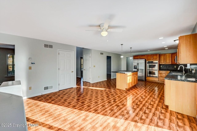 kitchen with stainless steel appliances, dark countertops, visible vents, and a sink