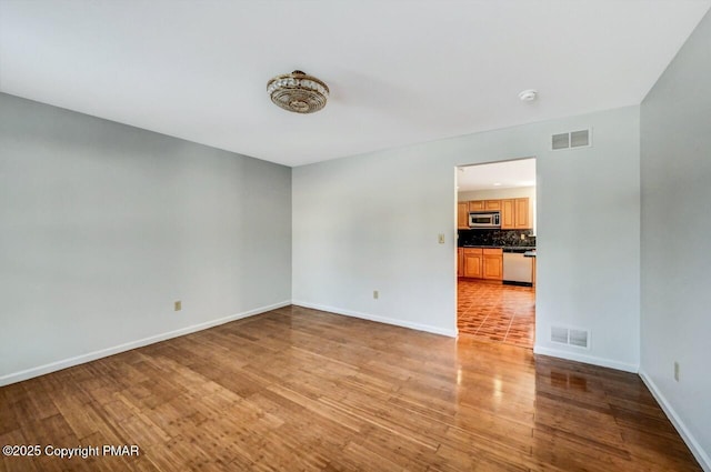 empty room with visible vents, light wood-style flooring, and baseboards