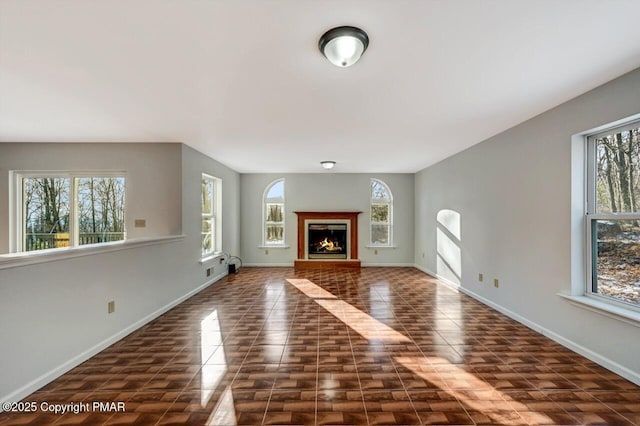 unfurnished living room with a brick fireplace, baseboards, and a wealth of natural light