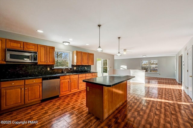 kitchen with a sink, appliances with stainless steel finishes, backsplash, a center island, and dark countertops