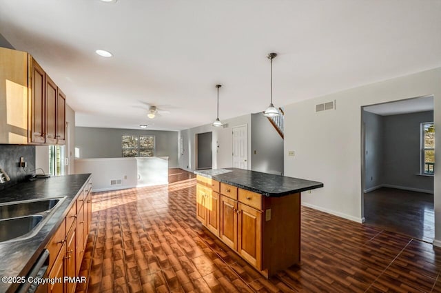 kitchen featuring open floor plan, dishwashing machine, dark countertops, and a sink