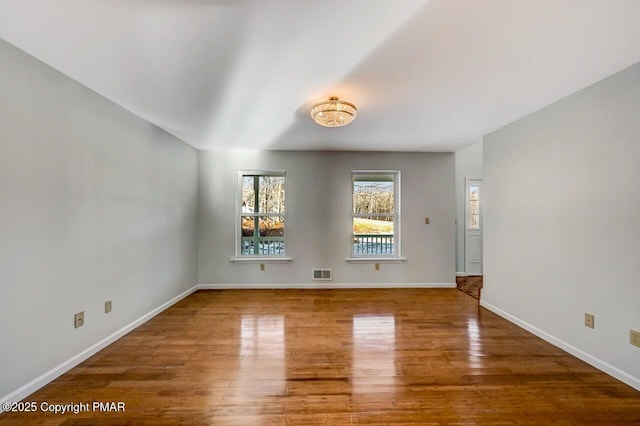 empty room featuring wood finished floors, visible vents, and baseboards