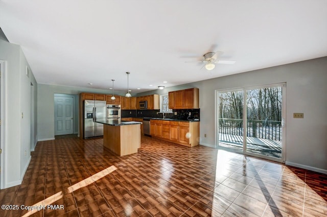 kitchen with dark countertops, appliances with stainless steel finishes, dark wood-style flooring, a center island, and backsplash