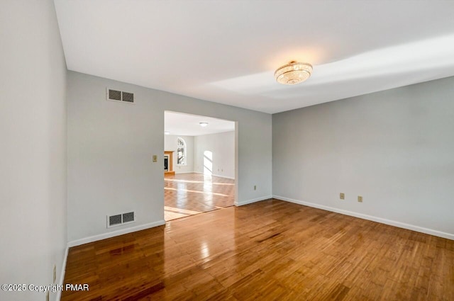 unfurnished room with a fireplace, wood finished floors, visible vents, and baseboards