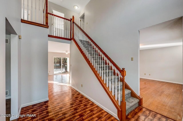 stairs with a towering ceiling, baseboards, and wood finished floors