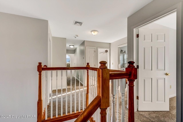 corridor with carpet floors, visible vents, and an upstairs landing