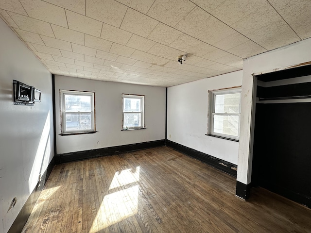 unfurnished bedroom with baseboards, multiple windows, and wood-type flooring