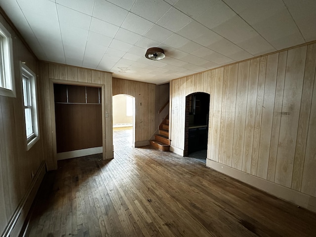 spare room featuring baseboards, arched walkways, hardwood / wood-style floors, and stairs