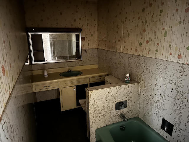 bathroom with wallpapered walls, a bath, vanity, and a wainscoted wall