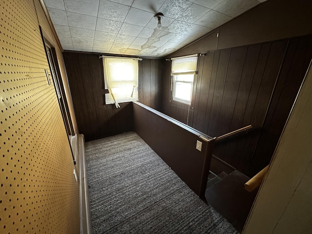 corridor featuring an upstairs landing, vaulted ceiling, wood walls, and carpet floors