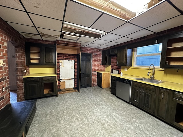 kitchen with brick wall, light floors, stainless steel dishwasher, a paneled ceiling, and a sink