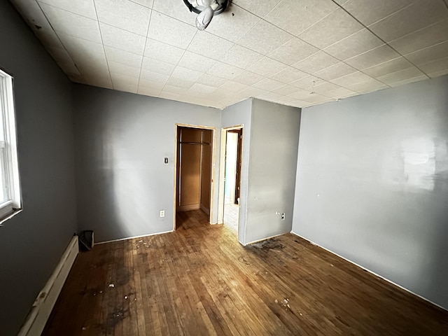 unfurnished bedroom featuring hardwood / wood-style floors, a walk in closet, a closet, and baseboard heating