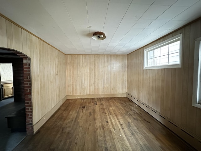 empty room with baseboards, wood walls, baseboard heating, arched walkways, and dark wood-style flooring