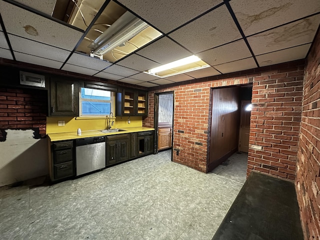 kitchen with light floors, brick wall, a sink, a paneled ceiling, and dishwasher