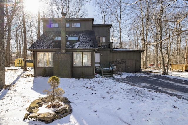 snow covered back of property with a balcony and a shed