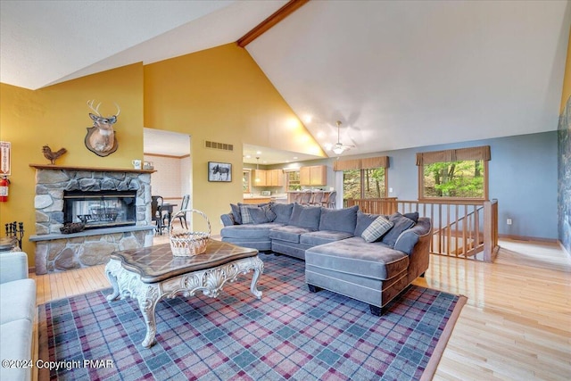 living area featuring a fireplace, visible vents, light wood-style flooring, high vaulted ceiling, and beamed ceiling